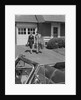 Couple carrying luggage walking towards convertible car in driveway by Anonymous