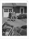 Couple carrying luggage walking towards convertible car in driveway by Anonymous