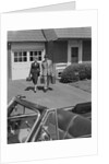 Couple carrying luggage walking towards convertible car in driveway by Anonymous