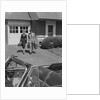 Couple carrying luggage walking towards convertible car in driveway by Anonymous