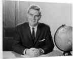 Smiling man sitting at desk with earth globe by Anonymous