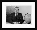Smiling man sitting at desk with earth globe by Anonymous