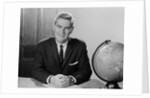Smiling man sitting at desk with earth globe by Anonymous