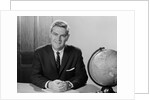 Smiling man sitting at desk with earth globe by Anonymous