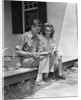 Man woman sitting on porch of farmhouse reading catalog by Anonymous