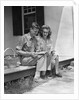 Man woman sitting on porch of farmhouse reading catalog by Anonymous