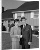 Couple smiling man and woman standing before suburban house by Anonymous