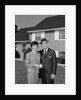 Couple smiling man and woman standing before suburban house by Anonymous