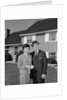 Couple smiling man and woman standing before suburban house by Anonymous