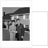 Couple smiling man and woman standing before suburban house by Anonymous