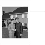Couple smiling man and woman standing before suburban house by Anonymous