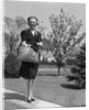 Stylishly dressed woman walking down suburban street carrying straw bag by Anonymous