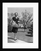 Stylishly dressed woman walking down suburban street carrying straw bag by Anonymous