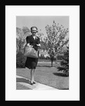 Stylishly dressed woman walking down suburban street carrying straw bag by Anonymous