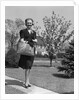 Stylishly dressed woman walking down suburban street carrying straw bag by Anonymous