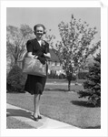 Stylishly dressed woman walking down suburban street carrying straw bag by Anonymous