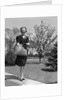 Stylishly dressed woman walking down suburban street carrying straw bag by Anonymous