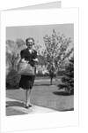 Stylishly dressed woman walking down suburban street carrying straw bag by Anonymous