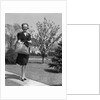 Stylishly dressed woman walking down suburban street carrying straw bag by Anonymous