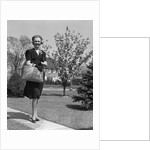 Stylishly dressed woman walking down suburban street carrying straw bag by Anonymous