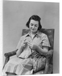 Brunette woman knitting sitting in armchair by Anonymous