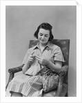Brunette woman knitting sitting in armchair by Anonymous