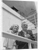 Smiling mature couple at shipboard rail with binoculars by Anonymous