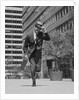 Businessman carrying briefcase holding his hat on running down urban sidewalk by Anonymous