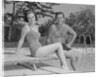 Man woman couple sitting on diving board on side of swimming pool by Anonymous