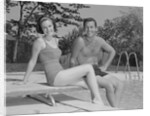 Man woman couple sitting on diving board on side of swimming pool by Anonymous