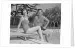 Man woman couple sitting on diving board on side of swimming pool by Anonymous