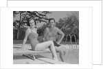 Man woman couple sitting on diving board on side of swimming pool by Anonymous