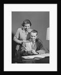 Couple man seated at desk holding paper woman standing looking over his shoulder smiling happy by Anonymous