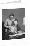 Couple man seated at desk holding paper woman standing looking over his shoulder smiling happy by Anonymous