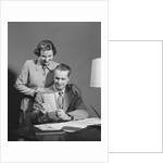 Couple man seated at desk holding paper woman standing looking over his shoulder smiling happy by Anonymous