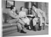 Couple sitting on couch talking to smiling insurance salesman handing them a policy by Anonymous