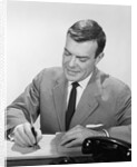 Smiling businessman at desk writing checks by Anonymous