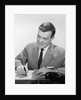 Smiling businessman at desk writing checks by Anonymous