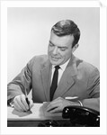 Smiling businessman at desk writing checks by Anonymous