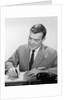 Smiling businessman at desk writing checks by Anonymous