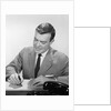 Smiling businessman at desk writing checks by Anonymous