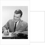 Smiling businessman at desk writing checks by Anonymous