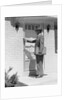 Salesman wearing suit tie hat carrying briefcase ringing suburban house doorbell by Anonymous