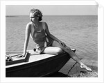 Woman wearing one piece bathing suit sitting on edge of boat by Anonymous