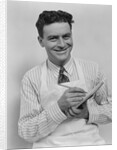 Smiling curly hair man wearing apron taking order with pencil and note pad by Anonymous