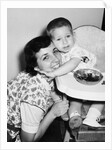 Baby boy hugging mother at dinner time, ca. 1953 by Anonymous
