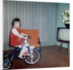 Young girl rides her new tricycle in the house, ca. 1967 by Anonymous