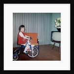 Young girl rides her new tricycle in the house, ca. 1967 by Anonymous