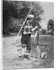 1950s boy plaid shirt sailor hat fishing pole dog pulling on tail of caught fish by Anonymous