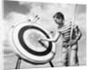 1960s boy jeans striped t-shirt holding bow & pulling arrow out of target bull's-eye by Anonymous